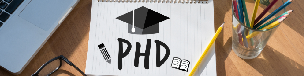 image with a laptop, a notepad with PhD written on it and some pencils in a jar